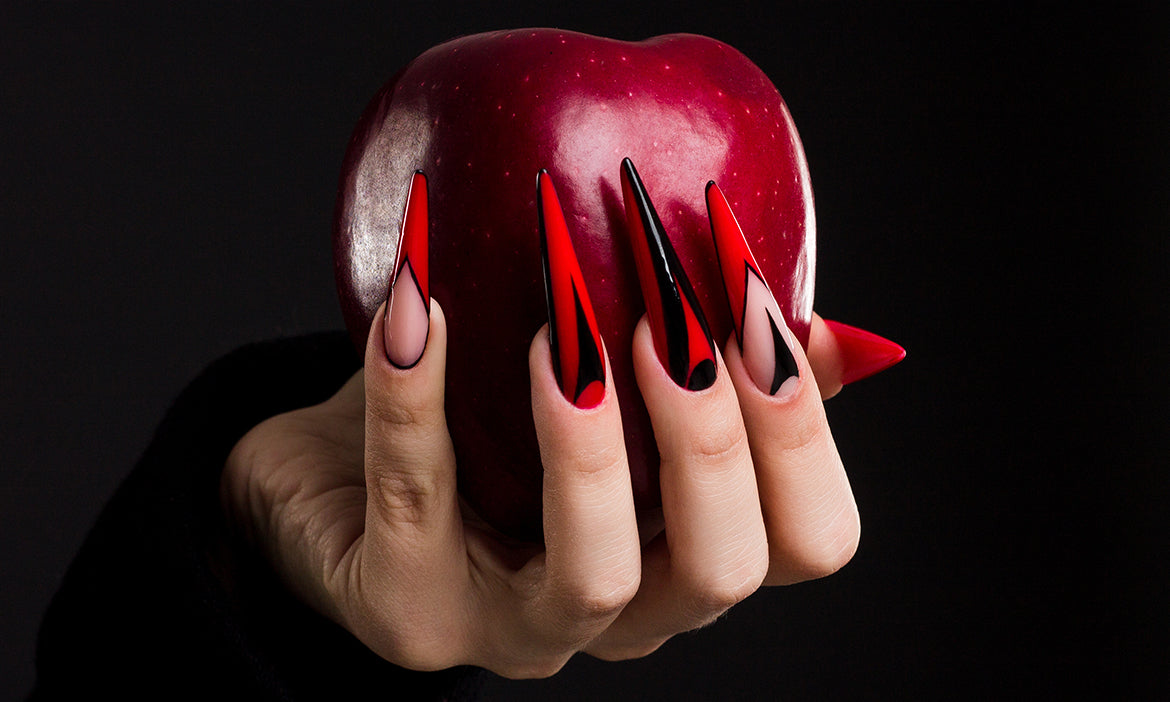 Hand with long red and black stiletto nails holding a shiny red apple against a black background.